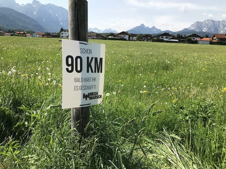 90-km-Wegweiser beim Megamarsch München Ein Wegweiser beim Megamarsch München. Er zeigt an, dass schon 90 km gewandert sind – nur noch 10 km bis ins Ziel in Mittenwald.